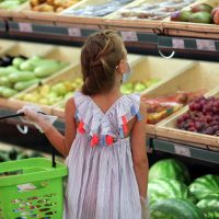 A girl in a medical mask in a supermarket buys vegetables and fruits. Social distancing, purchasing food safely COVID - 19 .